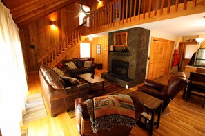 A cozy living room with a fireplace, wooden floors, a sofa set, and a dining area.