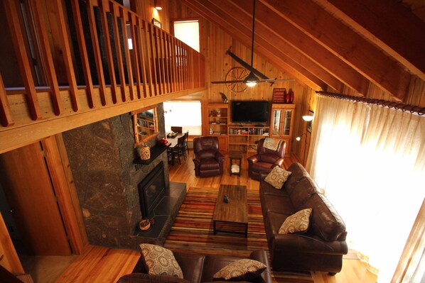 A spacious living room with a fireplace, leather sofas, a television, and a wooden ceiling.