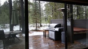 A deck with a grill and a table, overlooking a snowy forest. - Charming Cabin Near Fort Rock Park and SHARC! Hot Tub! 8 SHARC passes included! (Bend)
