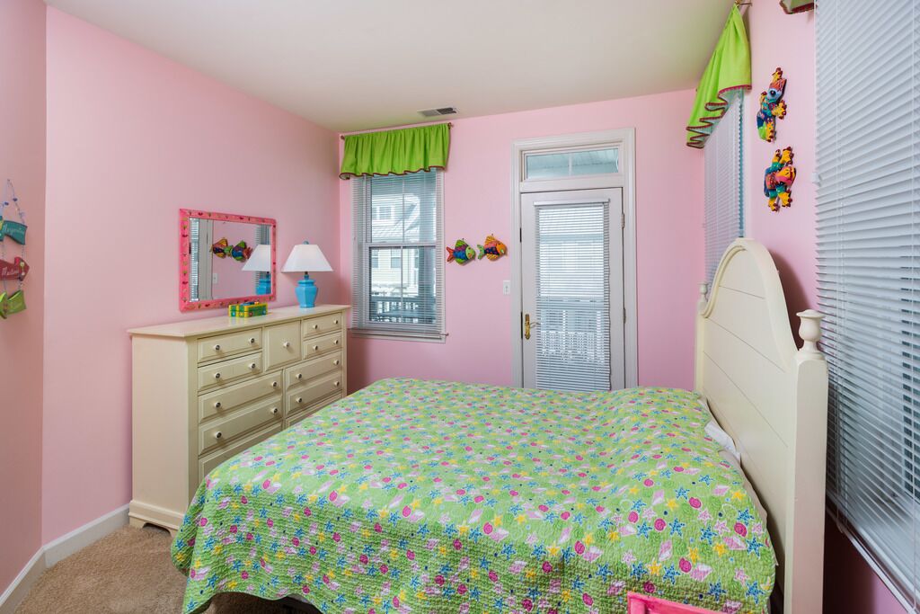 Un dormitorio rosa con cama, cómoda y ventana con persianas.