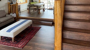 Un amplio espacio tipo loft con una escalera de madera, una mesa de comedor con bancos y un gran ventanal que ofrece vistas al exterior.
