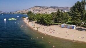 A beach with clear waters, a sandy shore, and a cityscape in the background.