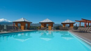 A swimming pool with lounge chairs and shaded areas, surrounded by mountains.