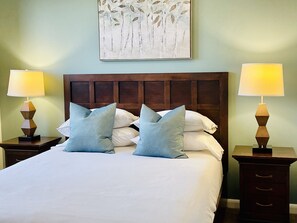 A neatly made bed with a wooden headboard, two bedside tables with lamps, and a wall art piece above the bed.
