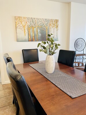 A dining table with a vase of green plants, black chairs, and a geometric patterned runner.