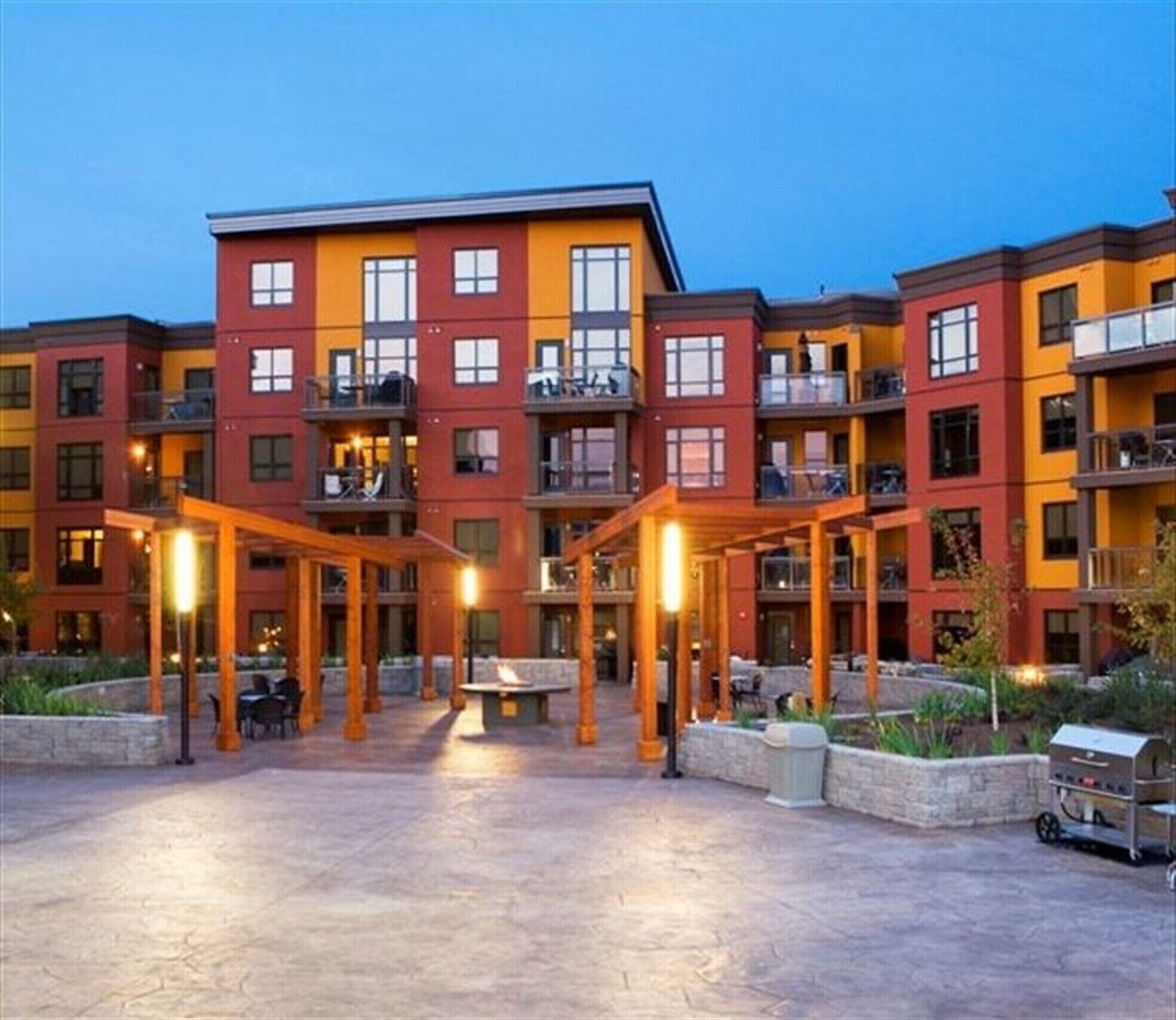 Un hotel de varios pisos con un patio, mobiliario exterior y una parrilla.