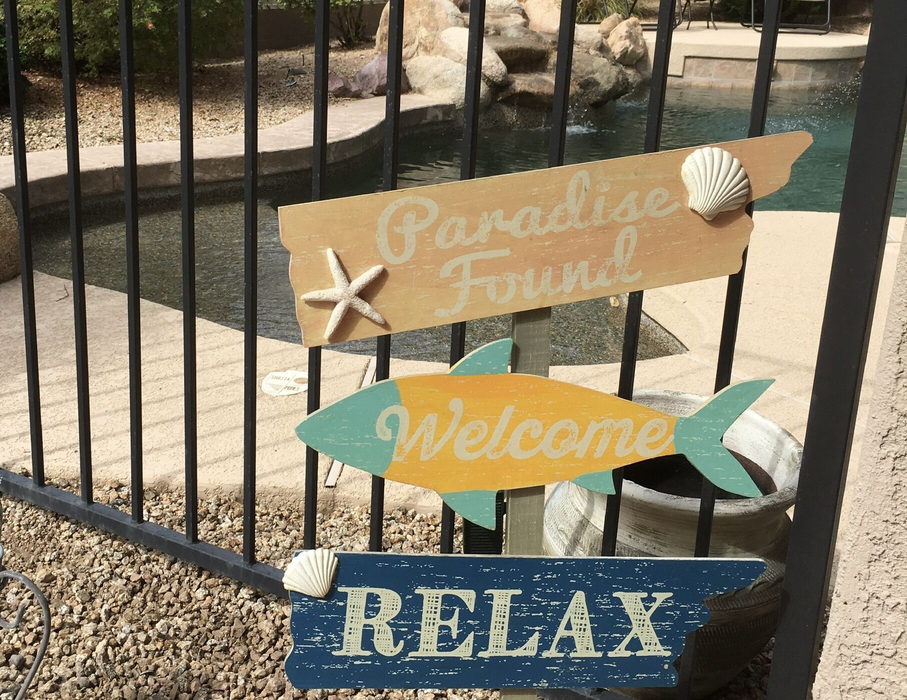 Un letrero con la inscripción 'Paradise Found' y 'Bienvenido', ubicado cerca de una piscina.