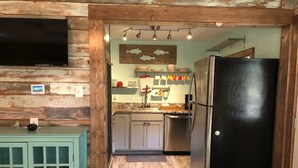 A kitchen with wooden walls, a stainless steel refrigerator, and a teal cabinet. - The Shell Cabin is a place to relax and enjoy the beach! (Port Aransas)
