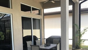 An outdoor patio area with a table and chairs, a ceiling fan, and large windows. - Model home in Lely Resort Naples Florida (Naples)