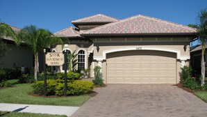 A residential house with a garage number 6472, a sign indicating 'Stock San Remo II Model', and a well-maintained front yard with plants and a paved driveway. - Model home in Lely Resort Naples Florida (Naples)