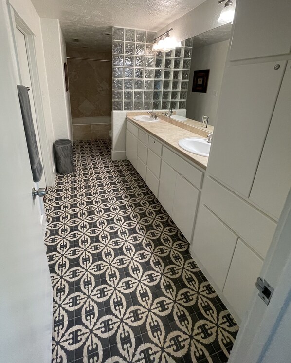 A bathroom with patterned black and white tiles, two sinks, a mirror, and a shower area.