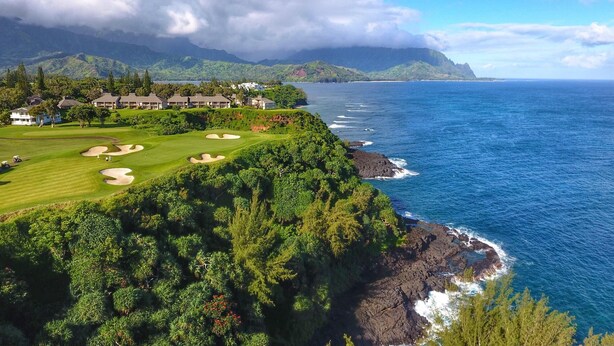 Un parcours de golf situé sur la côte, avec une végétation luxuriante, une vue dégagée sur l’océan et un paysage montagneux en toile de fond.