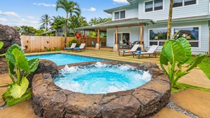 Un jardin avec un jacuzzi, des chaises longues et une maison.