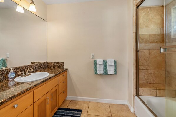 A bathroom with a granite countertop sink, wooden cabinets, a large mirror, and a glass shower enclosure.