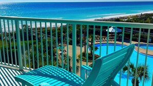 Ein Balkon mit türkisfarbenen Stühlen mit Blick auf einen Pool und Strand.
