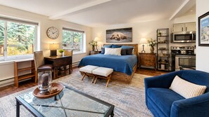 Une chambre à coucher comprenant un lit, des tables de chevet, un bureau, une chaise, une table basse et une vue sur l’extérieur.