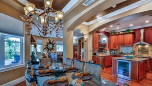 A spacious dining area with a large table set for a meal, a kitchen with modern appliances, and a view of the outdoors. - Casa Bahari W/Private Pool 5-Bed/Pool/Spa/Lux Amenities (Destin)
