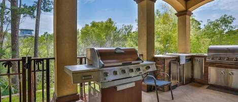 Un patio exterior con una parrilla y un lavamanos, rodeado de árboles y una zona cubierta.