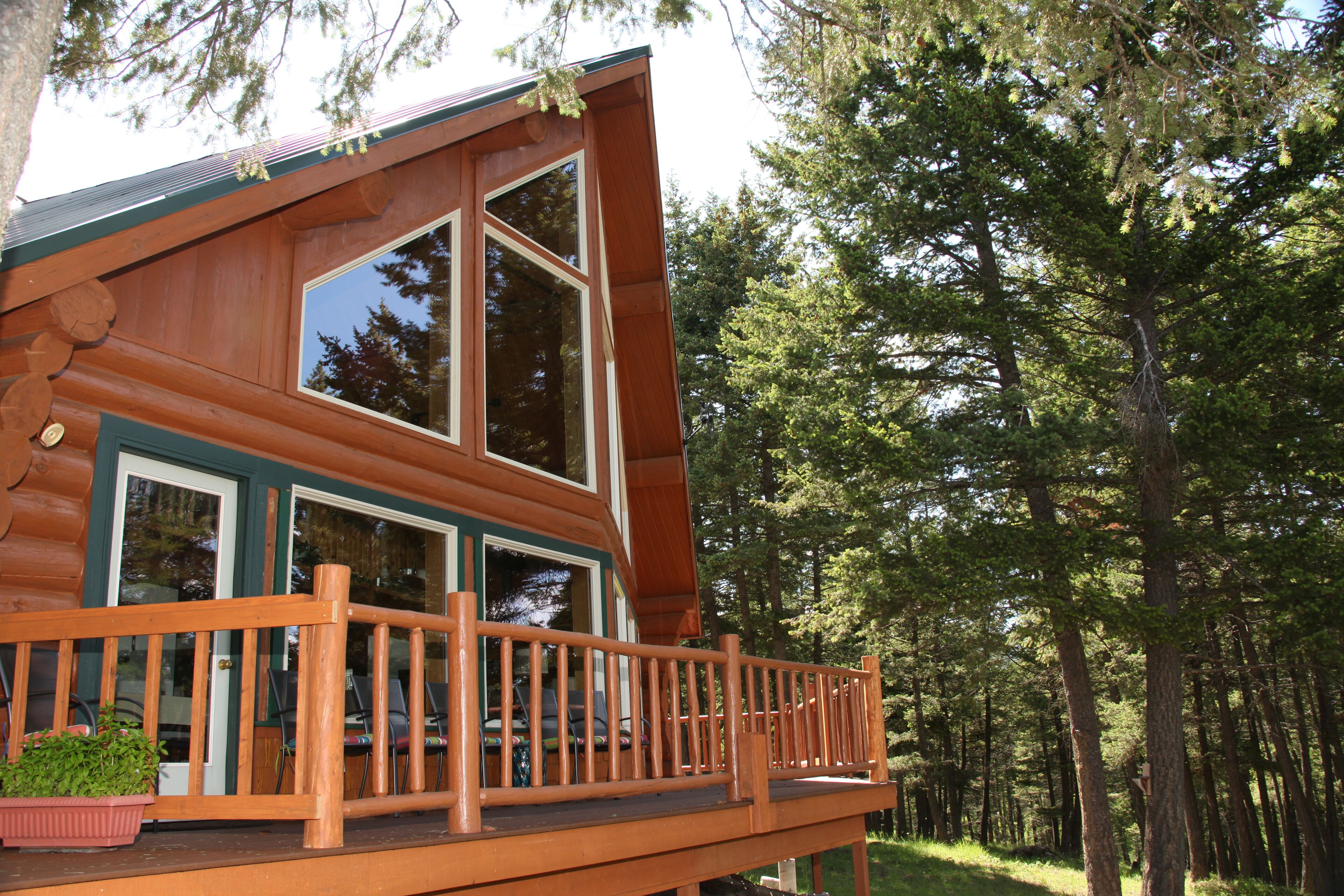 Une cabane en rondins dotée d’une terrasse en bois et de grandes fenêtres.