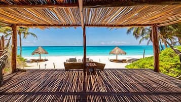 A beach view from a covered area with a wooden floor, two lounge chairs, and a table.
