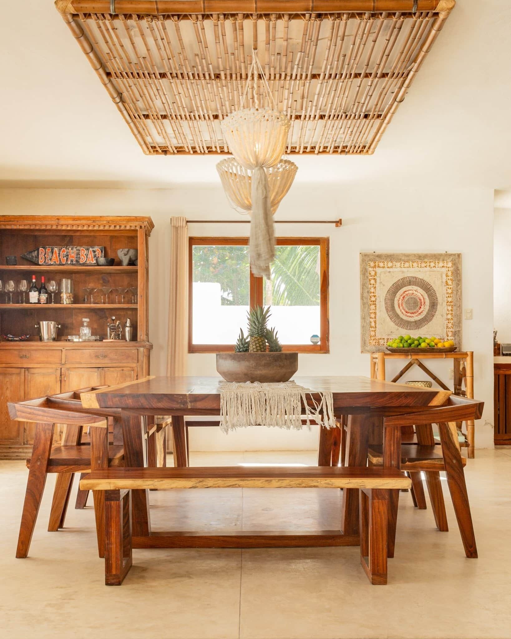 A spacious dining area with a large wooden table, a hanging bamboo ceiling, and a view of the outdoors through a window.