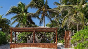 A beachside lounge with white cushioned seating, a wooden table with a bottle of champagne, and a thatched roof structure. - Casa Carolina Tulum (Tulum)