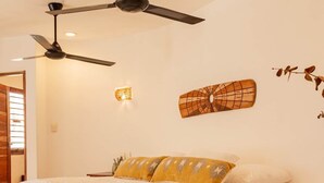 A bedroom with a bed, a ceiling fan, a wall-mounted light, and a decorative wall piece. - Casa Carolina Tulum (Tulum)