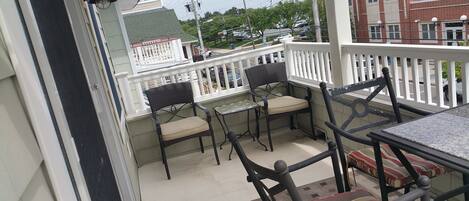 A balcony with outdoor furniture, including chairs and a table, and a view of the street and buildings in the background.