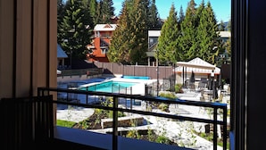 Blick auf einen Poolbereich mit eingezäuntem Deck, umgeben von Bäumen und Gebäuden.