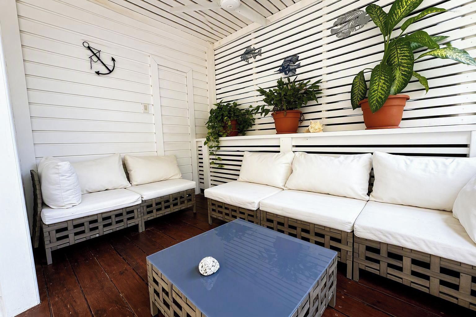 A cozy outdoor seating area with two white cushioned sofas and a small table, surrounded by wooden railings and potted plants.
