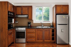 Eine Küche mit Holzausstattung, einem Edelstahlkühlschrank, einem Herd und einem Fenster mit Blick auf Grünflächen.