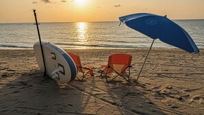 En strandscen med en surfbräda, två strandstolar och ett blått parasoll.