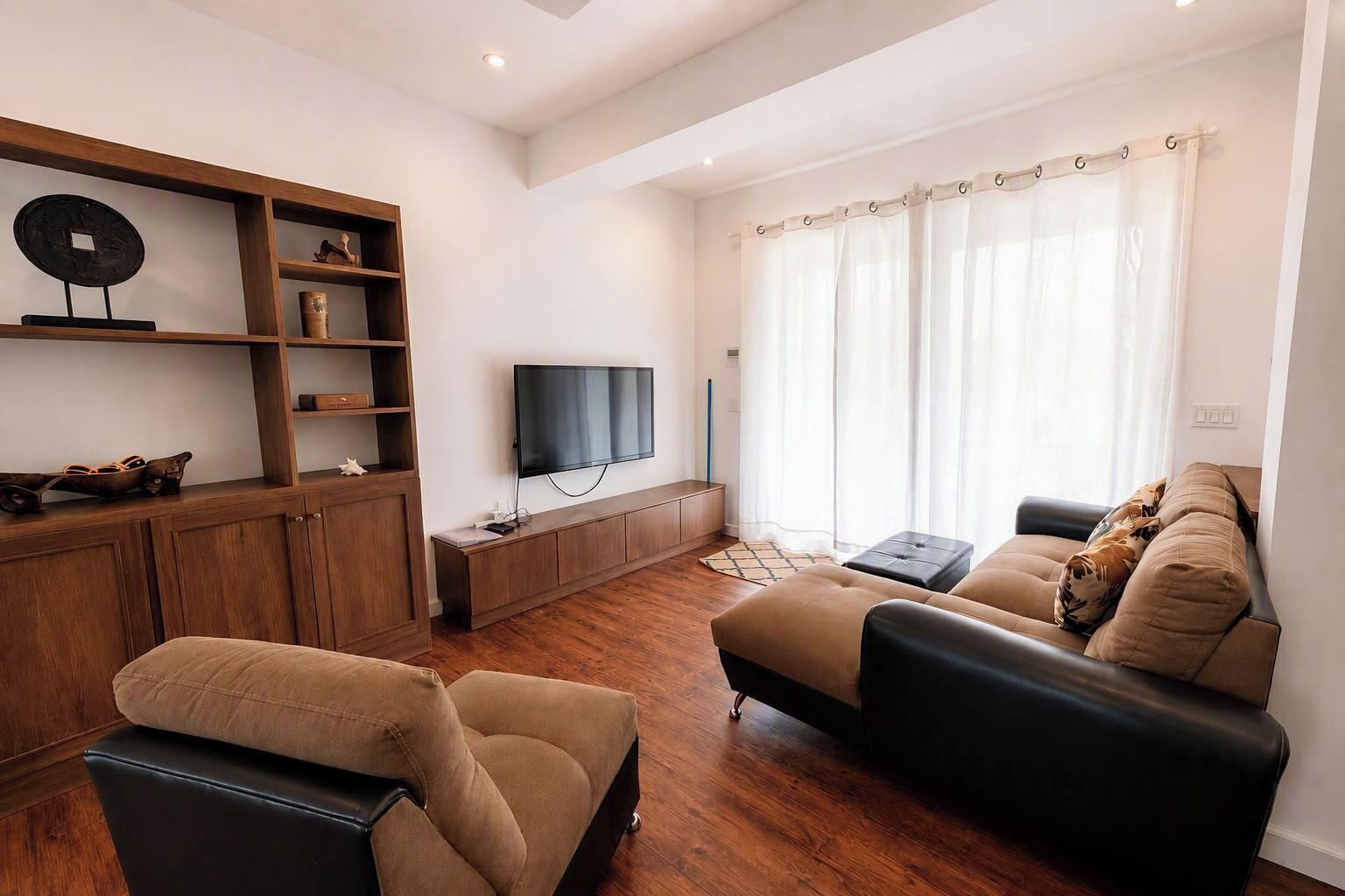 A modern living room with a sofa, a television, wooden shelving, and a window with curtains.