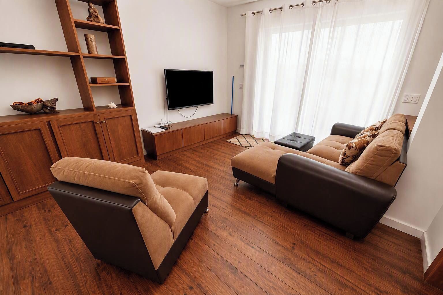 A modern living room with a sofa set, wooden flooring, a flat-screen TV, and a wooden cabinet.