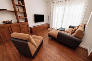 Una sala de estar moderna con un conjunto de sofá, piso de madera, televisor de pantalla plana y un mueble de madera.