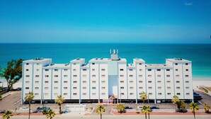 A multi-story hotel with a central entrance, located near a beach with clear blue waters. - Right on the Gulf! Beautiful white sandy beachfront! Safe, quiet, and friendly! (Treasure Island)
