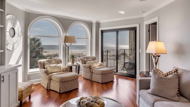 A spacious living room with a large window overlooking the beach, furnished with patterned chairs and a sofa. - "Sea Escape" ~ Fully Renovated ~ Beach Gear credit included ~ Pool Access (Isle of Palms)