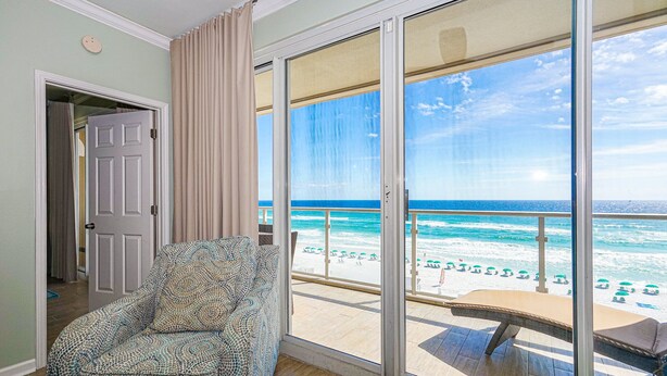 Une pièce dotée d’une grande porte-fenêtre coulissante donnant sur un balcon avec vue sur la plage et l’océan.