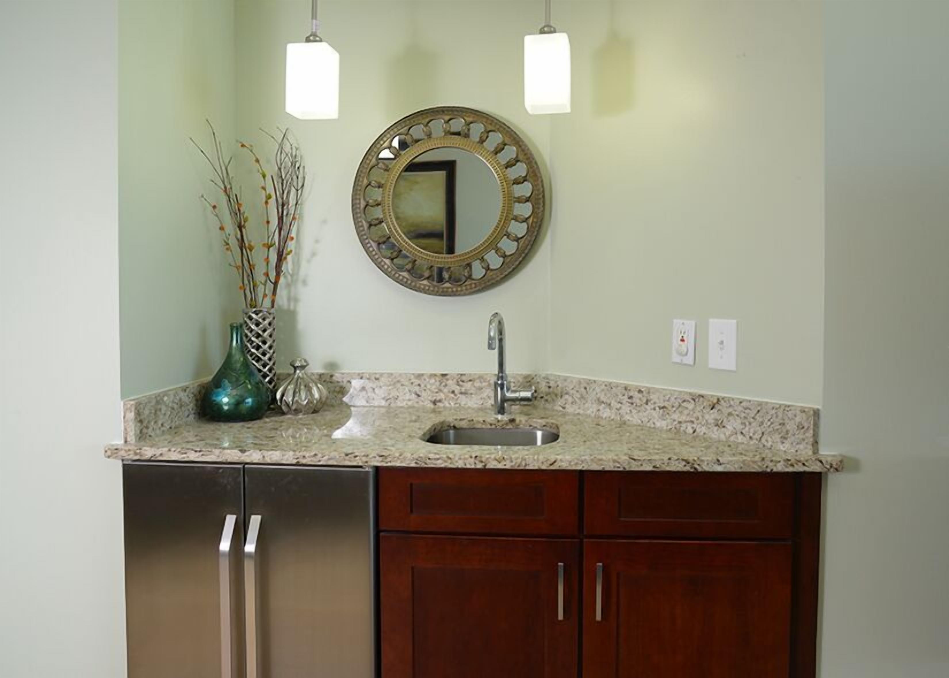 A kitchen with a granite countertop, stainless steel sink, wooden cabinets, and a decorative mirror.