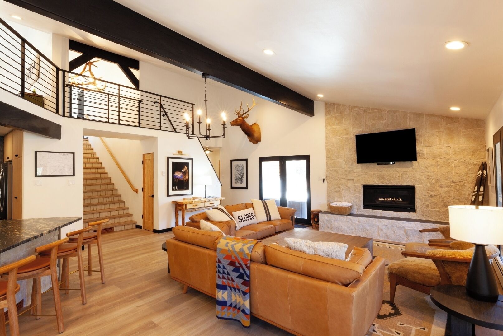 Ein geräumiger Wohnbereich mit hoher Decke, einer Treppe, einem Kamin und einem an der Wand befestigten Fernseher.