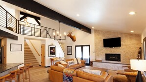 A spacious living area with a high ceiling, a staircase, a fireplace, and a mounted television.
