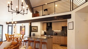 A modern kitchen with a central island, wooden bar stools, and a dining area with a sofa and chairs.