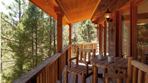 A wooden deck with a table and chairs, overlooking a forest.
