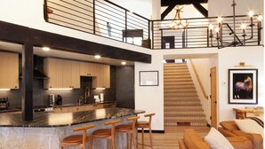 A modern kitchen with a central island, bar stools, and a staircase leading to a loft area.