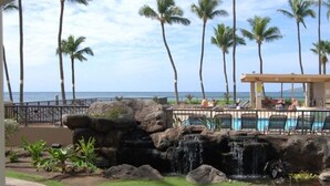 A pool area with lounge chairs, a waterfall feature, and palm trees. - Sugar Beach Resort  - Ocean View,   (Off Season Special Rates) (Kihei)