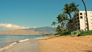 A beach with a building, palm trees, and mountains in the background. - Sugar Beach Resort  - Ocean View,   (Off Season Special Rates) (Kihei)