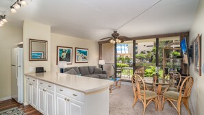 A modern kitchen with a central island, white cabinetry, and a dining area with wicker chairs and a glass table. - Sugar Beach Resort  - Ocean View,   (Off Season Special Rates) (Kihei)