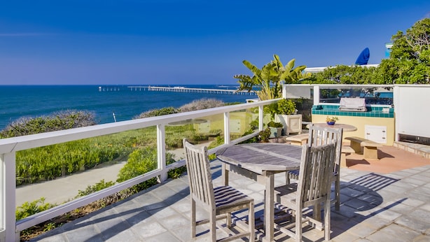 A terrace with a table and chairs, overlooking a coastal view with a pier in the distance.