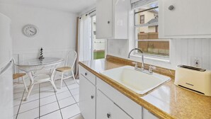 Una cuina amb armaris blancs, un rentamans, una torradora i una zona de menjador amb taula i cadires.