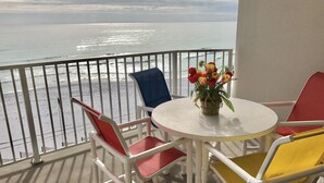 Un balcón con una mesa y sillas blancas, un jarrón de flores y vista al océano.